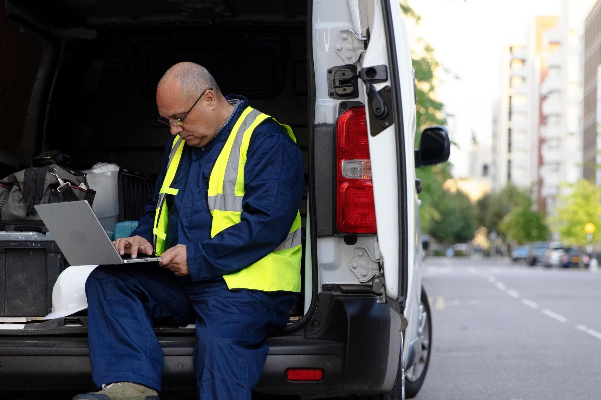 Technician in a safety vest sits in an open van while working on a laptop.
